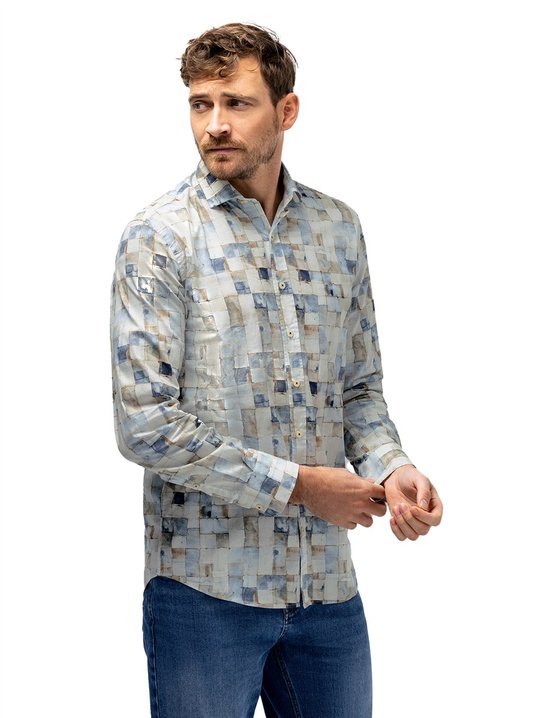 Man met donker haar, baard en snor, draagt een blauw-bruin blokkerig overhemd en spijkerbroek, mouwen oprollend.