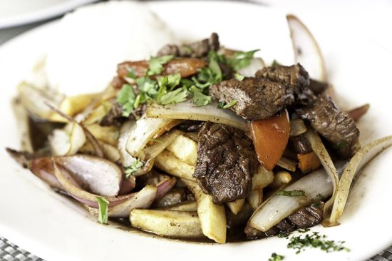 Bord Lomo Saltado met rundvlees, frietjes, ui, tomaat en koriander.