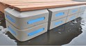 Grijze modulaire vlonder met blauwe accenten, met houten dek. Drie lagen stootranden aan de zijkant.