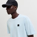 Man met donkere huid draagt lichtblauwe t-shirt en zwarte pet, detail van het label.