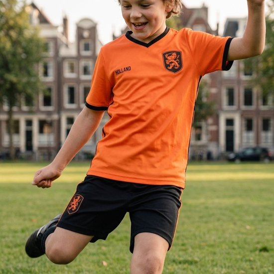 Jongen in oranje voetbaltenue, dribbelend met bal op een grasveld.