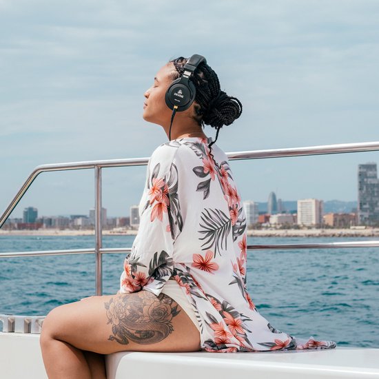 Vrouw met gevlochten haar draagt zwarte Devine koptelefoon op een boot, met een bloemenprint kimono.