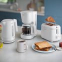 Bouilloire, cafetière et grille-pain Philips blancs sur un plan de travail avec un croissant et des toasts.