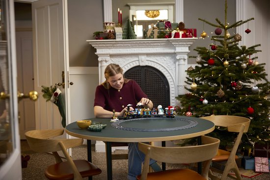 Vrouw zit aan tafel en bouwt aan een LEGO-trein voor Kerstmis, bij een kerstboom.