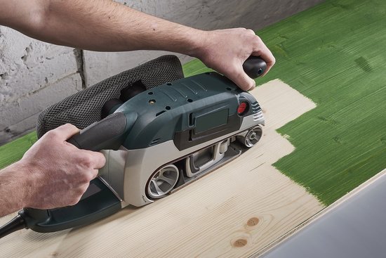 Groene schuurmachine met één band wordt gebruikt op een lichtgroen geverfd houten oppervlak.
