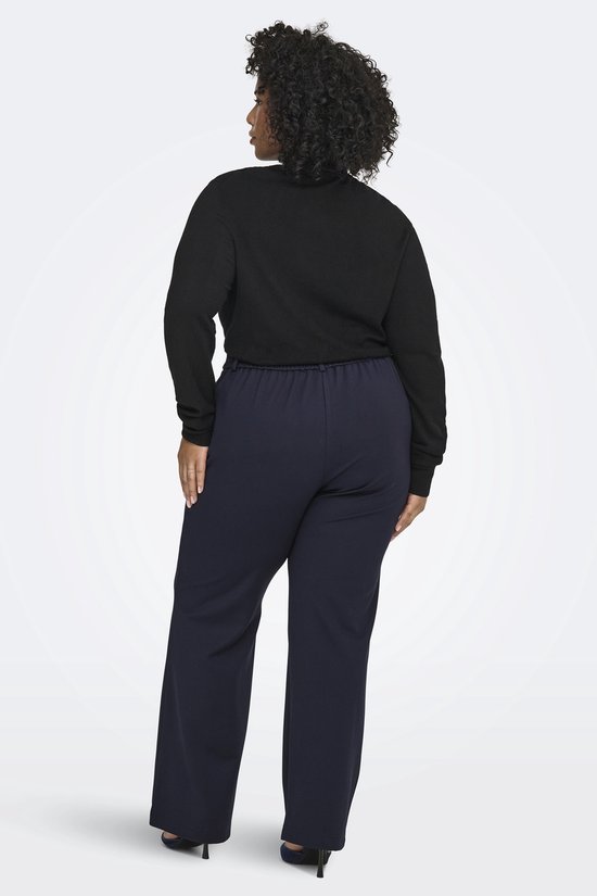 Model van achteren gezien, draagt donkerblauwe broek met wijde pijpen en zwarte coltrui.