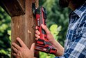 Man met rood-zwarte multitool werkt aan een houten paal.