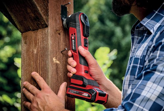 Man met rood-zwarte multitool werkt aan een houten paal.
