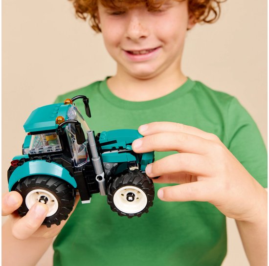 Jongen houdt een felgroene tractor vast met grote zwarte banden en witte velgen.