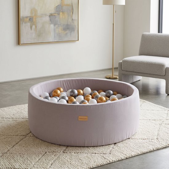Ronde, taupe grijze ballenbak met gouden, zilveren en parelmoer ballen. Staat op een beige geruit kleed.