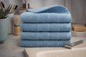Pile de quatre serviettes bleu clair sur un lavabo en marbre, avec des accessoires de salle de bain.