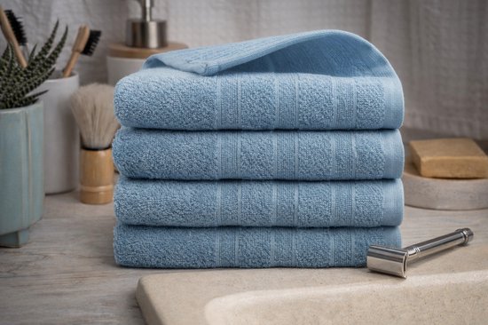 Pile de quatre serviettes bleu clair sur un lavabo en marbre, avec des accessoires de salle de bain.