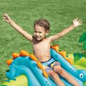 Een jongen met zijn armen omhoog zit op een blauwe dinosaurusglijbaan in een opblaasbaar zwembad.
