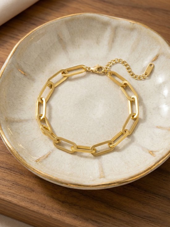 Gouden schakelarmband met rechthoekige schakels in een beige schaaltje.