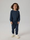 Jongen in een donkerblauwe trui met V-hals en rond label, en bijpassende joggingbroek.