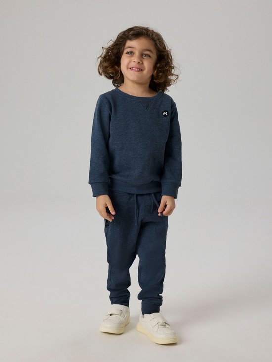 Jongen in een donkerblauwe trui met V-hals en rond label, en bijpassende joggingbroek.