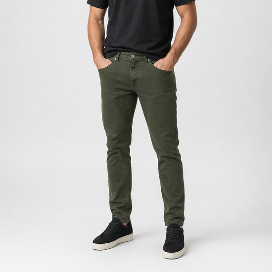 Een man met handen in zakken van een groene corduroy broek, met zwarte sneakers.
