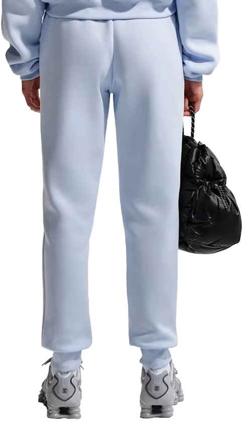 Dames joggingbroek van Nike in lichtblauw, met zwarte tas in de hand.