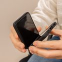 Handen die een open zwarte opklapbare telefoonhoes vasthouden.