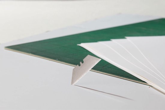 Een close-up van een mesje dat uit een stapel witte papieren wordt gehaald, met een groene snijmat op de achtergrond.