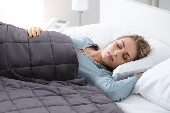Vrouw slaapt onder een grijze verzwaringsdeken op een wit bed.