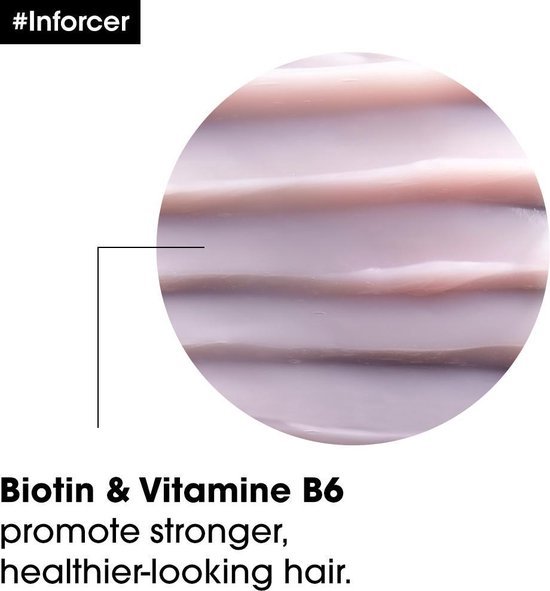 Close-up van de textuur van een lichtroze crème met de tekst "Biotine & Vitamine B6 bevorderen sterker, gezonder haar".
