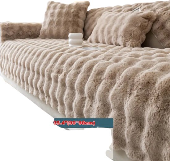 Un canapé beige et moelleux à la texture côtelée. Trois coussins et un objet sont visibles sur le canapé.