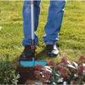 Man met blauwe jeans en zwarte schoenen gebruikt de turquoise graskantafsteker bij planten.