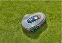 Grijze robotmaaier met turkooizen accenten op een groen gazon.