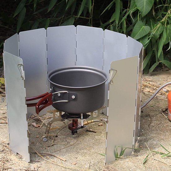 Aluminium windscherm om een kampeerfornuis met pan op zand, buiten.