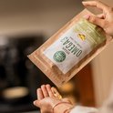 Handen houden een papieren zak van 'Ekopura Vegan Omega 3 Algae Oil' vast, met capsules die in de handpalm vallen.