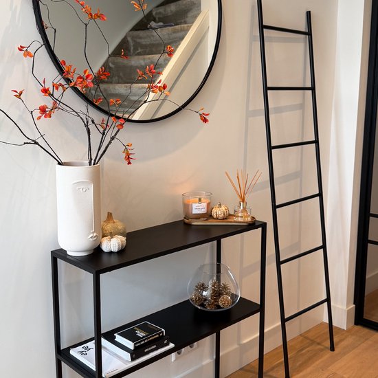 Zwarte decoratieve ladder naast een zwarte consoletafel met herfstdecoratie.