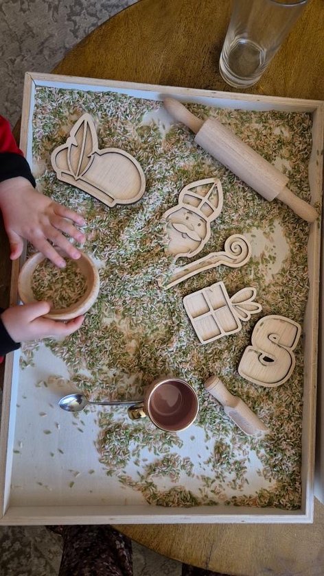 Kinderspeelbak met gekleurde rijst en houten Sint Nicolaas thema figuren, een deegroller en een beker.