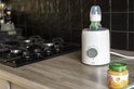Witte Alecto flessenwarmer met een babyfles op een aanrecht, naast een potje babyvoeding.