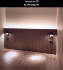 Twee zwarte wandlampen aan een houten lambrisering, die sfeervol licht werpen op de muur en vloer.