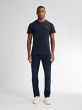 Man in een donkerblauw T-shirt en een donkerblauwe jeans met witte sneakers.