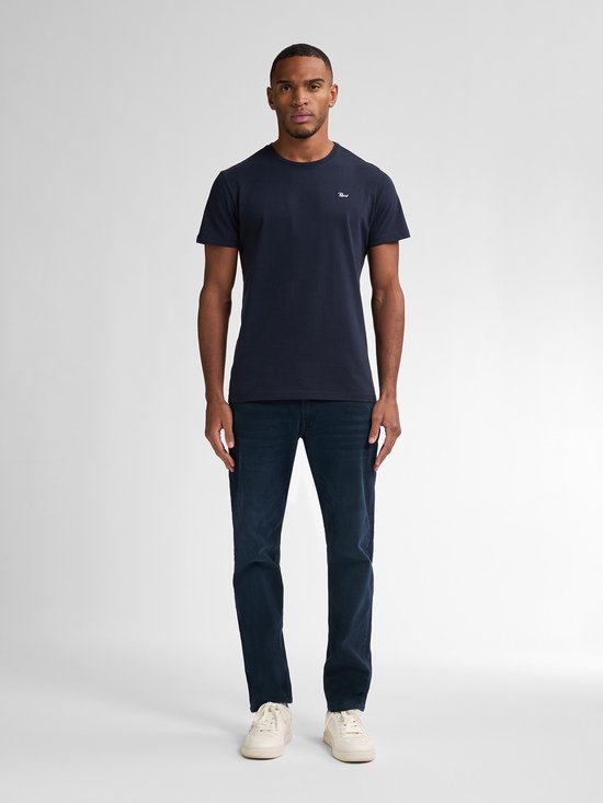 Man in een donkerblauw T-shirt en een donkerblauwe jeans met witte sneakers.