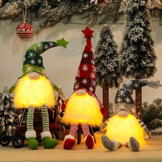 Trois gnomes de Noël assis et éclairés, devant un décor hivernal avec des sapins.