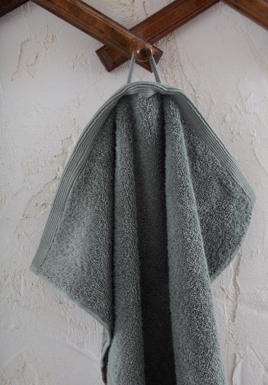 Lichtgroene handdoek hangt aan een kapstok aan een rustiek ogende muur.