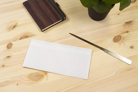 Een briefopener ligt naast een witte envelop op een houten bureau. Een notitieboekje en plant staan ernaast.