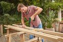Man met bril en roze hemd boort in houten balken met een groene Bosch accuboorschroevendraaier.
