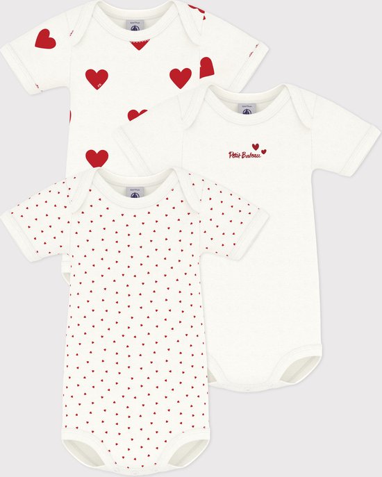 Drie witte rompertjes met korte mouwen, waarvan één met grote rode hartjes, één met kleine rode hartjes en één effen wit met 'Petit Bateau' logo.