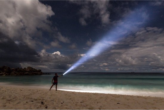 Man op een strand bij nacht die een krige lichtbundel schijnt met een zwarte zaklamp.