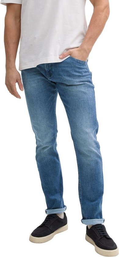 Man draagt een blauwe jeans met opgerolde broekspijpen en witte sneakers.