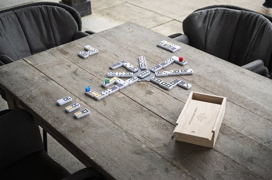 Een groep mensen speelt Mexican Train domino op een houten tafel buiten, met een open kist.