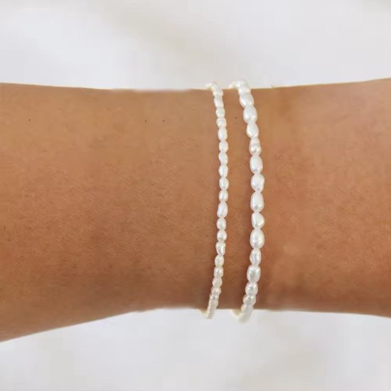 Twee dunne armbanden van witte parels, gedragen om een arm.