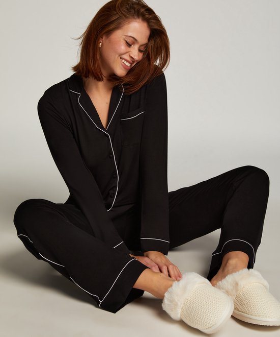 Model zittend met zwart nachthemd met witte biezen en witte pantoffels.