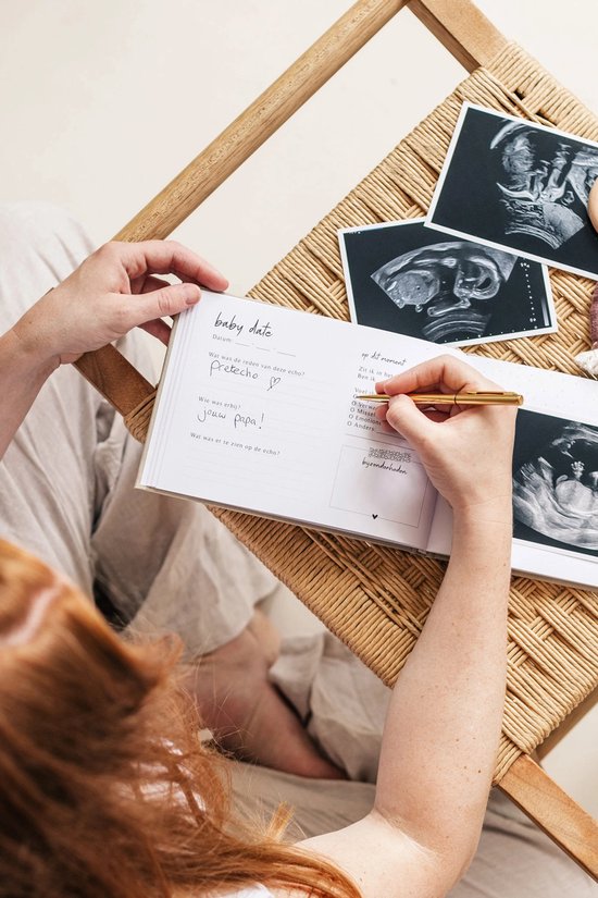 Een vrouw met rood haar schrijft in een boekje met echo's van een baby ernaast.