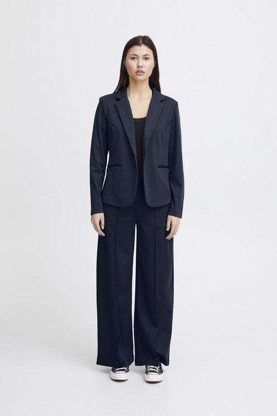 Een vrouw met lang donker haar draagt een marineblauwe blazer met een zwarte top en wijde, marineblauwe broek.