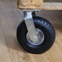Zwart luchtband zwenkwiel met zilverkleurige metalen steun, gemonteerd op een houten pallet.